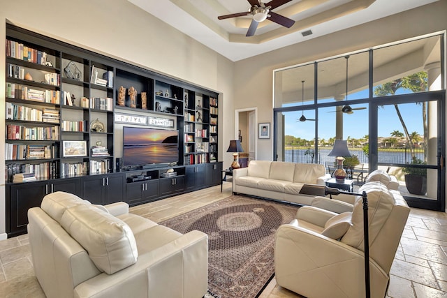 living room featuring ceiling fan, a high ceiling, and a tray ceiling