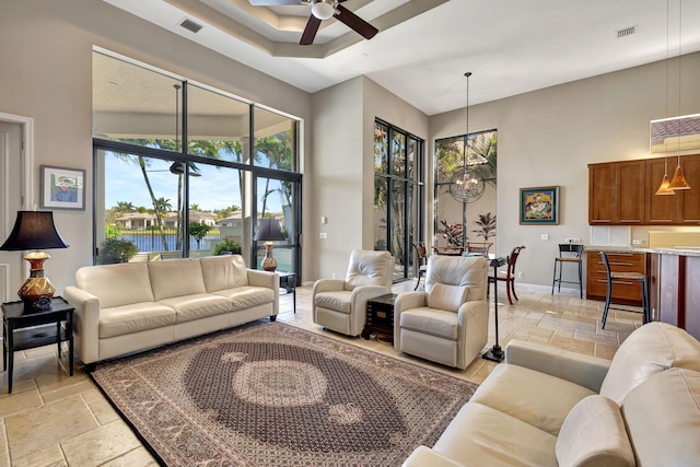 living room with ceiling fan with notable chandelier, a water view, and a towering ceiling