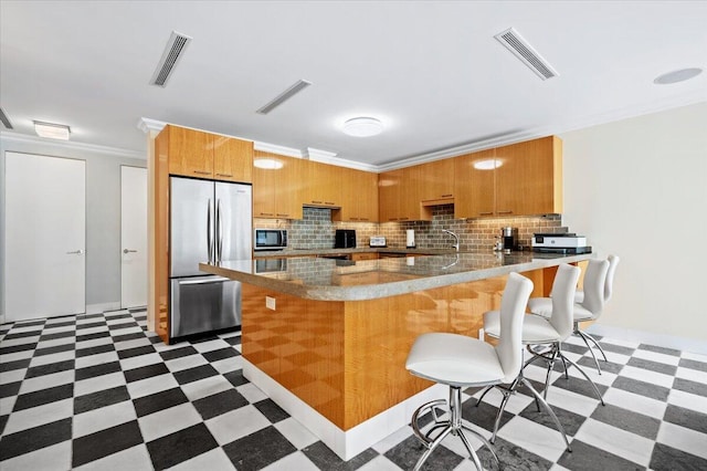 kitchen with a kitchen breakfast bar, decorative backsplash, ornamental molding, appliances with stainless steel finishes, and kitchen peninsula