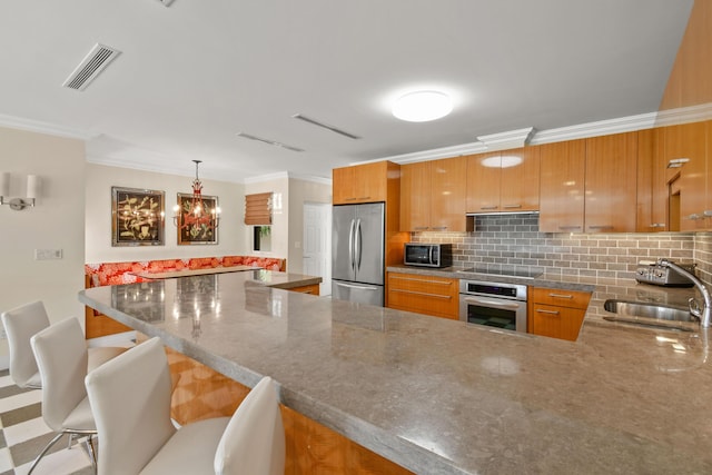 kitchen with pendant lighting, sink, crown molding, a kitchen bar, and stainless steel appliances