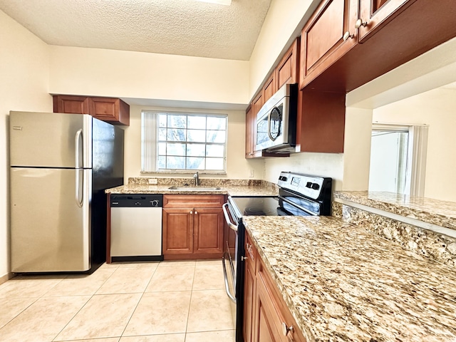 kitchen featuring light stone countertops, sink, a textured ceiling, light tile patterned floors, and appliances with stainless steel finishes