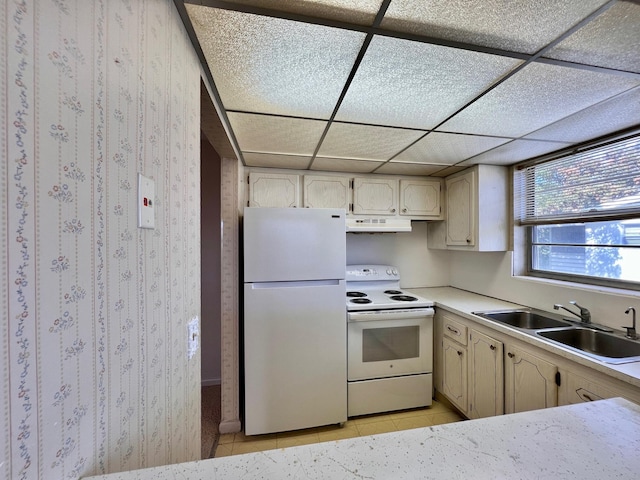 kitchen with light tile patterned floors, a sink, white appliances, a drop ceiling, and under cabinet range hood