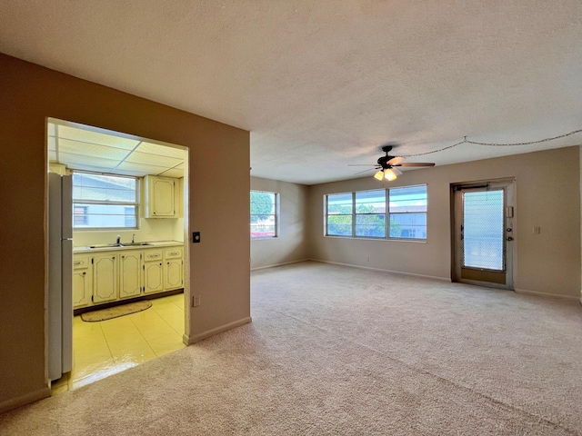 unfurnished room featuring light carpet, a textured ceiling, baseboards, and a ceiling fan