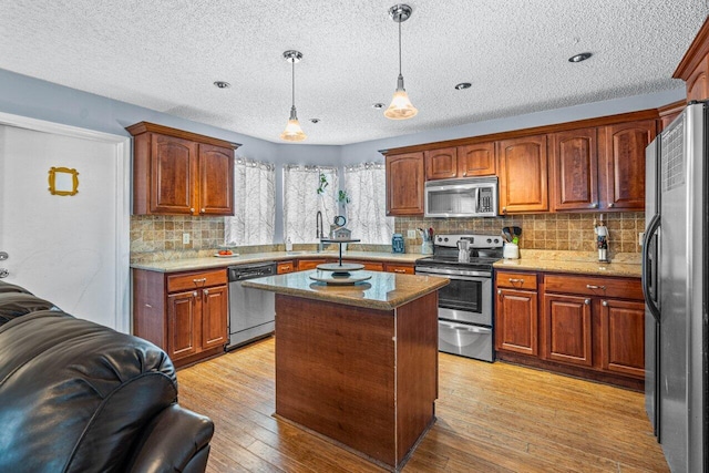 kitchen with a textured ceiling, light wood-type flooring, stainless steel appliances, and hanging light fixtures