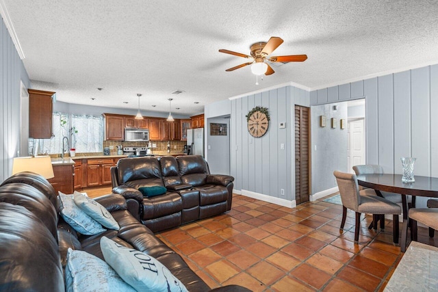 tiled living room featuring wood walls, sink, ceiling fan, ornamental molding, and a textured ceiling