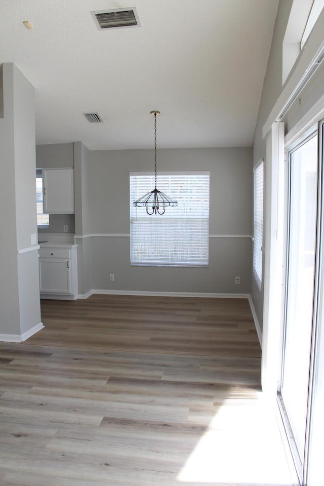 unfurnished dining area with a chandelier, vaulted ceiling, light hardwood / wood-style flooring, and a healthy amount of sunlight