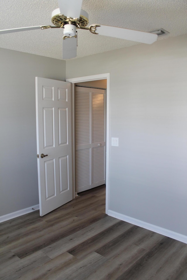 unfurnished bedroom with a textured ceiling, dark hardwood / wood-style floors, and ceiling fan