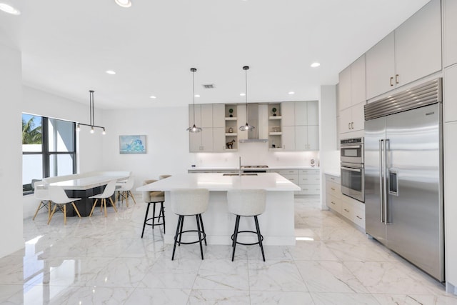 kitchen with a center island with sink, hanging light fixtures, a breakfast bar area, gray cabinets, and stainless steel appliances