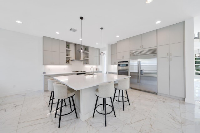 kitchen featuring a kitchen breakfast bar, stainless steel appliances, a large island with sink, decorative light fixtures, and gray cabinets