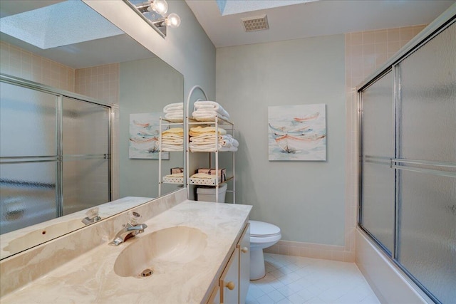 full bathroom with combined bath / shower with glass door, a skylight, vanity, tile patterned flooring, and toilet