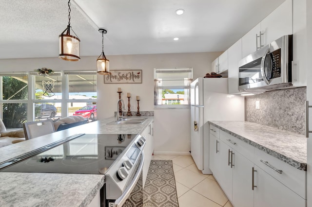 kitchen featuring a sink, stainless steel microwave, tasteful backsplash, freestanding refrigerator, and range with electric stovetop