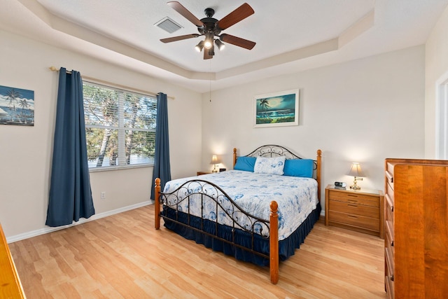 bedroom with a tray ceiling, ceiling fan, and light hardwood / wood-style flooring