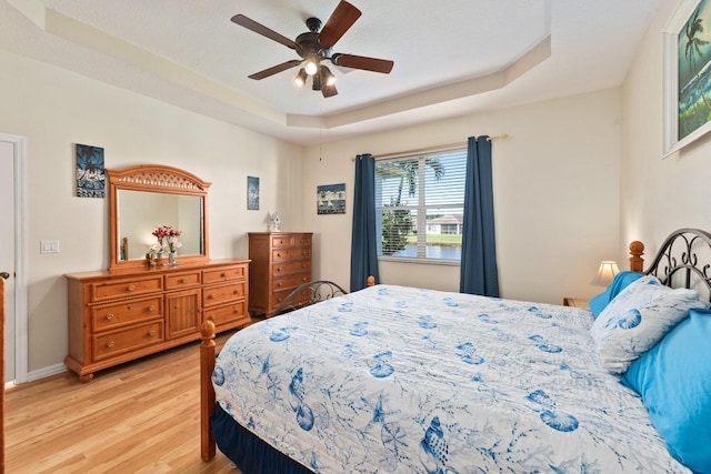 bedroom with ceiling fan, a raised ceiling, and light hardwood / wood-style flooring