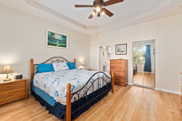 bedroom with a raised ceiling, ceiling fan, ensuite bathroom, and light hardwood / wood-style floors