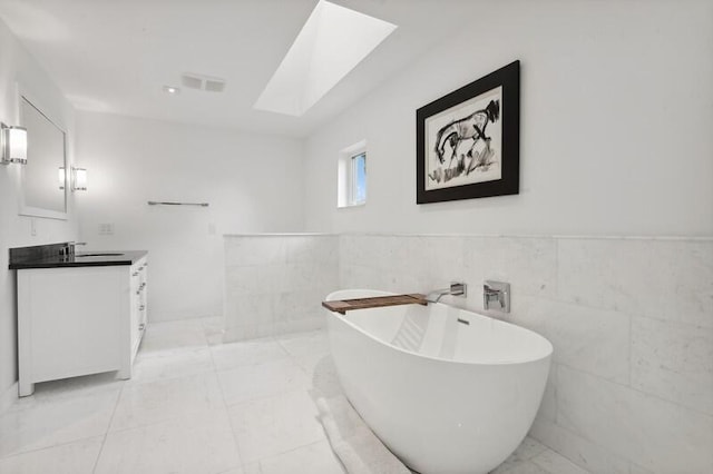 bathroom with tile patterned floors, vanity, a skylight, tile walls, and a bathtub