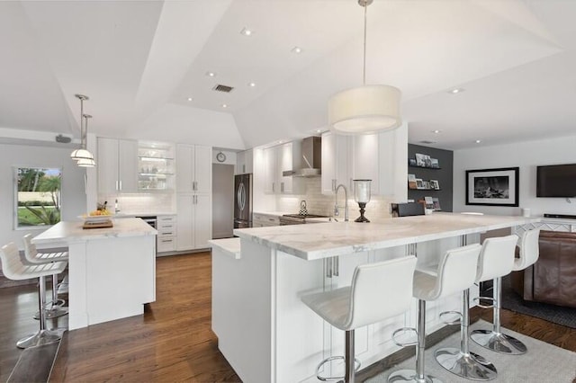 kitchen with backsplash, kitchen peninsula, hanging light fixtures, white cabinets, and wall chimney exhaust hood