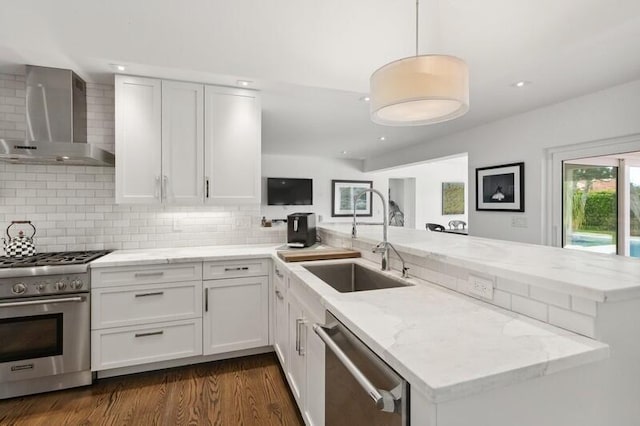 kitchen featuring wall chimney range hood, kitchen peninsula, sink, appliances with stainless steel finishes, and white cabinets