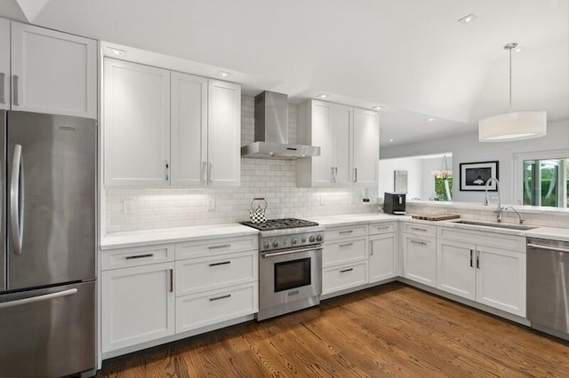 kitchen featuring appliances with stainless steel finishes, white cabinetry, wall chimney range hood, decorative backsplash, and sink