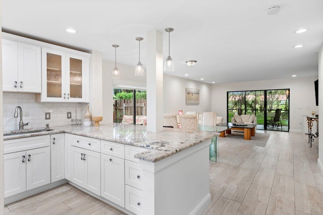 kitchen with open floor plan, decorative backsplash, a peninsula, white cabinets, and a sink