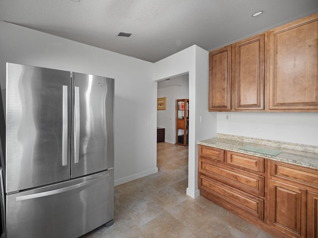 kitchen featuring light stone countertops and stainless steel refrigerator