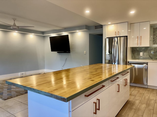 kitchen with appliances with stainless steel finishes, ceiling fan, white cabinets, a center island, and butcher block counters