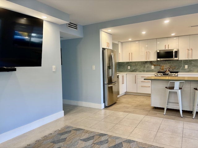 kitchen featuring a kitchen breakfast bar, kitchen peninsula, decorative backsplash, appliances with stainless steel finishes, and white cabinetry