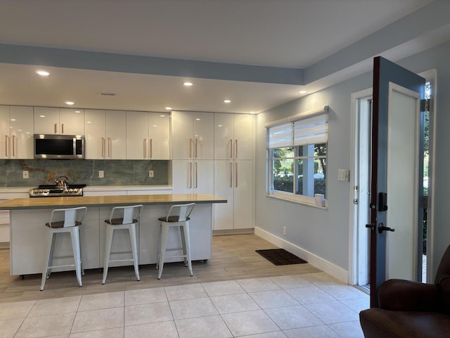 kitchen with a kitchen bar, tasteful backsplash, light tile patterned floors, white cabinets, and range