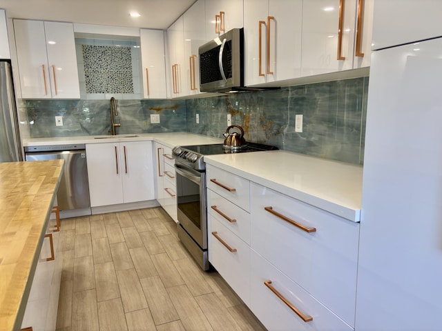 kitchen featuring backsplash, white cabinetry, wooden counters, and stainless steel appliances