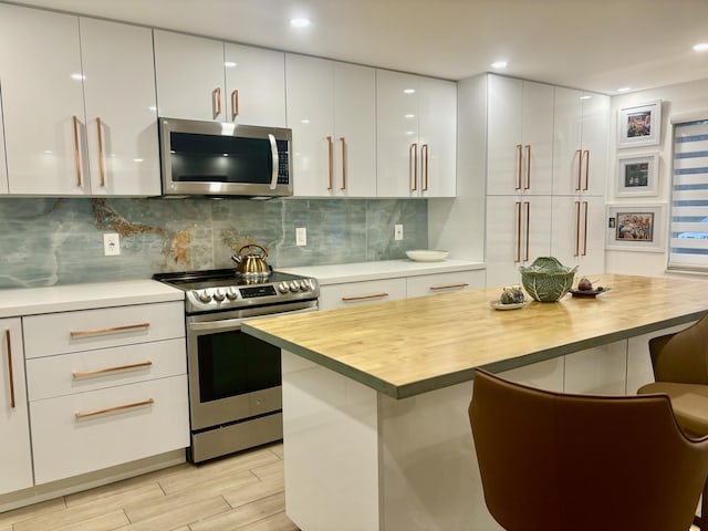 kitchen featuring appliances with stainless steel finishes, backsplash, a breakfast bar, white cabinets, and butcher block counters