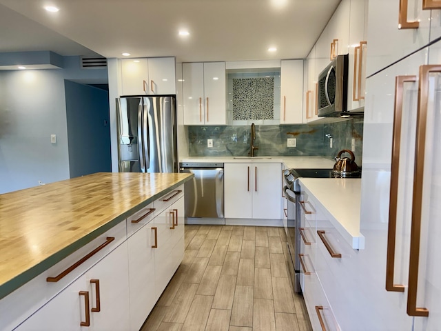 kitchen with white cabinetry, sink, light hardwood / wood-style flooring, backsplash, and appliances with stainless steel finishes