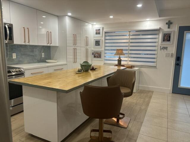 kitchen featuring white cabinetry, stainless steel appliances, wood counters, decorative backsplash, and a breakfast bar