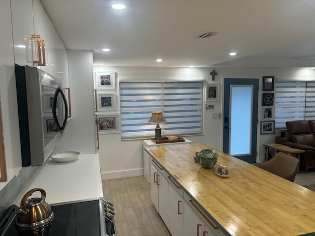 kitchen with white cabinets, butcher block counters, and stainless steel stove