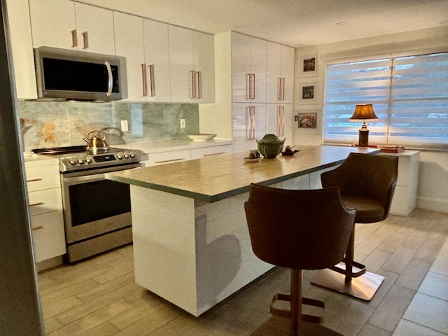 kitchen featuring a breakfast bar, white cabinets, tasteful backsplash, a kitchen island, and stainless steel appliances