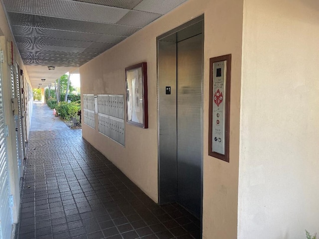 corridor with dark tile patterned flooring, mail area, and elevator