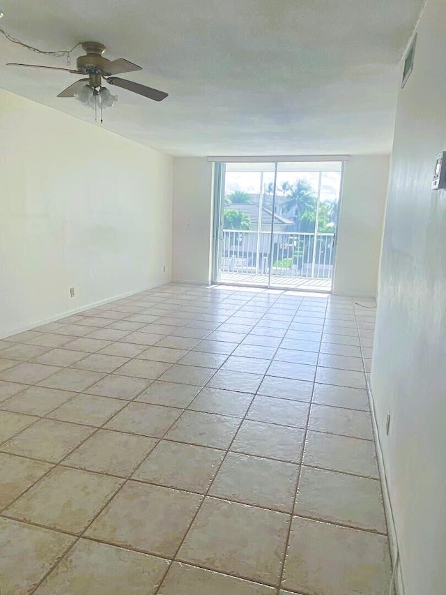 empty room featuring light tile patterned floors, visible vents, ceiling fan, a wall of windows, and baseboards