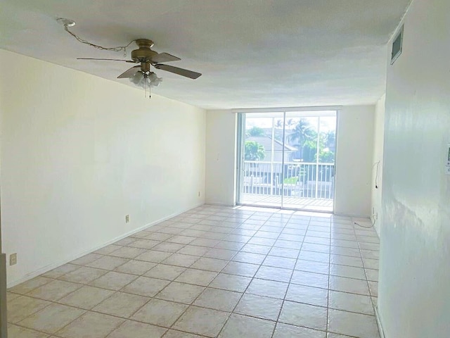 empty room featuring a ceiling fan, expansive windows, light tile patterned flooring, and visible vents