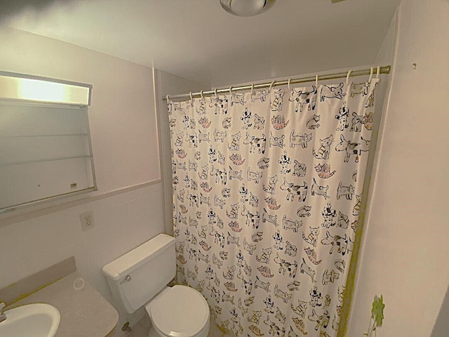 bathroom featuring a wainscoted wall, tile walls, a shower with shower curtain, toilet, and a sink