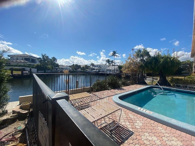 pool featuring a patio, a water view, and fence