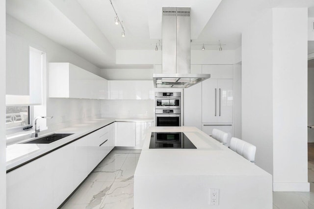 kitchen with sink, a breakfast bar area, stainless steel double oven, white cabinetry, and island exhaust hood