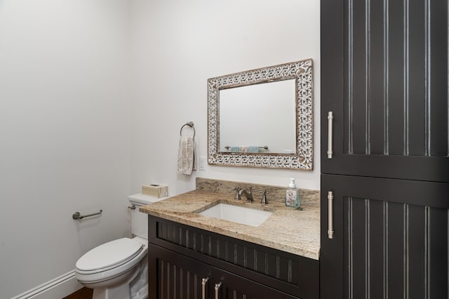 half bath with baseboards, vanity, and toilet