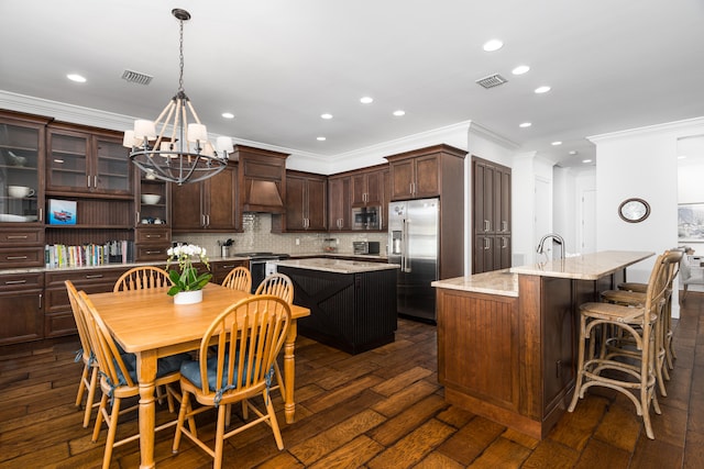 kitchen featuring light stone countertops, a center island with sink, visible vents, and built in appliances