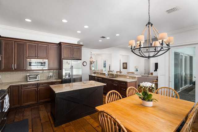 kitchen featuring decorative light fixtures, appliances with stainless steel finishes, a sink, a kitchen island, and light stone countertops