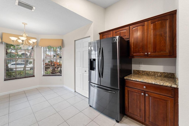 kitchen with light tile patterned flooring, stainless steel refrigerator with ice dispenser, an inviting chandelier, and light stone counters