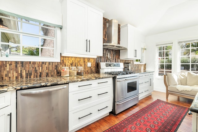 kitchen with white cabinetry, wall chimney exhaust hood, stainless steel appliances, backsplash, and wood-type flooring