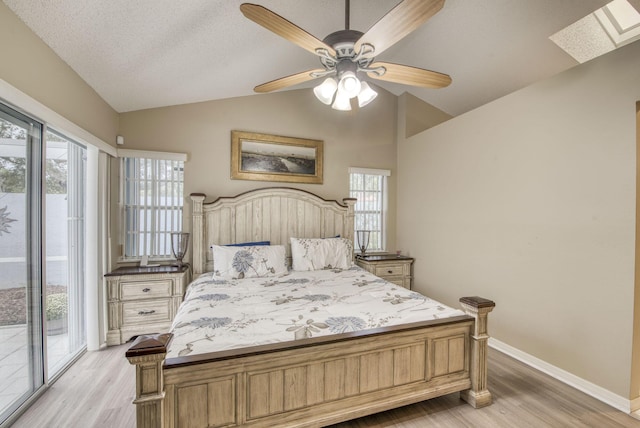 bedroom with access to exterior, vaulted ceiling, light wood finished floors, baseboards, and a skylight