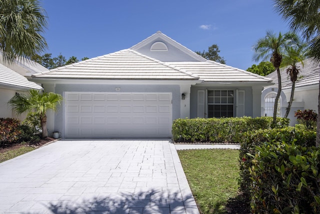 ranch-style home featuring stucco siding, decorative driveway, an attached garage, and a tiled roof