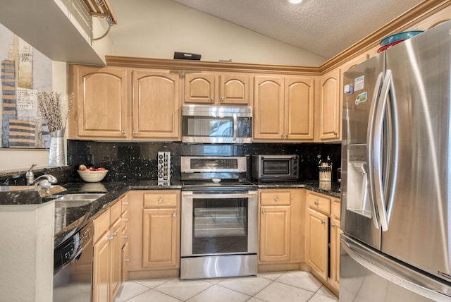kitchen featuring appliances with stainless steel finishes, light brown cabinetry, a sink, light tile patterned flooring, and lofted ceiling