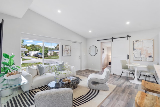 living room featuring a barn door, light hardwood / wood-style floors, and high vaulted ceiling