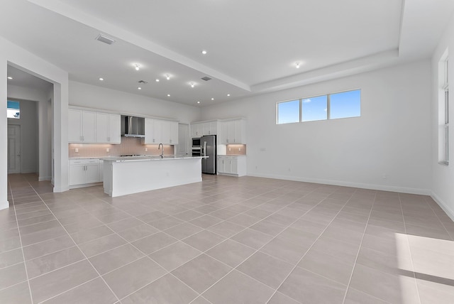 kitchen featuring a kitchen island with sink, white cabinets, wall chimney exhaust hood, light tile patterned floors, and stainless steel appliances