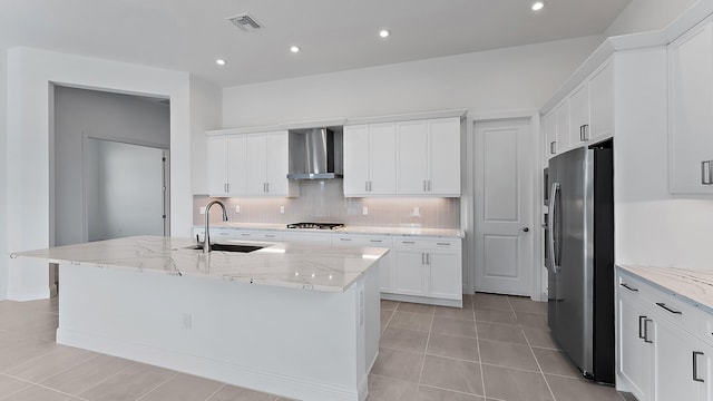 kitchen with white cabinets, wall chimney exhaust hood, an island with sink, light stone counters, and stainless steel appliances